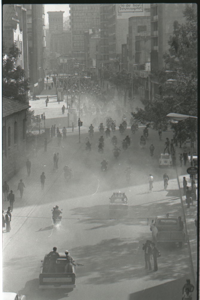 Ciclismo, Nacional de turismeros, Bogotá- La Calera, Sopó-Zipaquirá, junio 24, 1979. Una icónica calle bogotana, la carrera séptima, cubierta en polvo e inundada, esta vez, no por la lluvia (como en tantas fotografías de Caicedo) sino por decenas de ciclistas y acompañantes. Esta imagen recuerda la gran tradición fotográfica deportiva que podemos remontar incluso hasta Lartigue y su fascinación por el movimiento capturado en escenas composicionalmente muy cuidadas y atmosféricas.