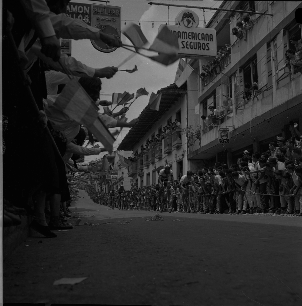 Ciclismo, Vuelta a Colombia, Medellín-Anserma, Cochise pasando por Quebrada, marzo 30, 1965. Los ciclistas fueron posiblemente, los primeros héroes deportivos colombianos. Caicedo se encargó repetidamente de presentar al país la imagen de estos nuevos héroes nacionales y el efecto avasallante de un público que sencillamente los adoraba.