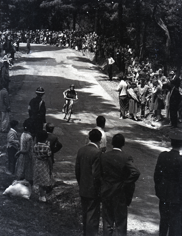 Ciclista descendiendo en bicicleta. Esta imagen ejemplifica dos de los motivos que Caicedo resalto reiteradamente en su fotografía ciclística: su fascinación por el vértigo y las demandas sensorias a las que son expuestos los ciclistas; y el público que encuentra en este deporte una de las eventos sociales más importantes en la conformación de signos de identidad nacional.