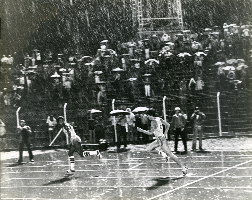 Corredores bajo la lluvia. En esta imagen se unen varios de los temas favorecidos por el lente de Caicedo la lluvia, los deportes, la noche, todos ellos articulados a través de una iluminación cenital que brinda a la imagen un carácter teatral y atmosférico.