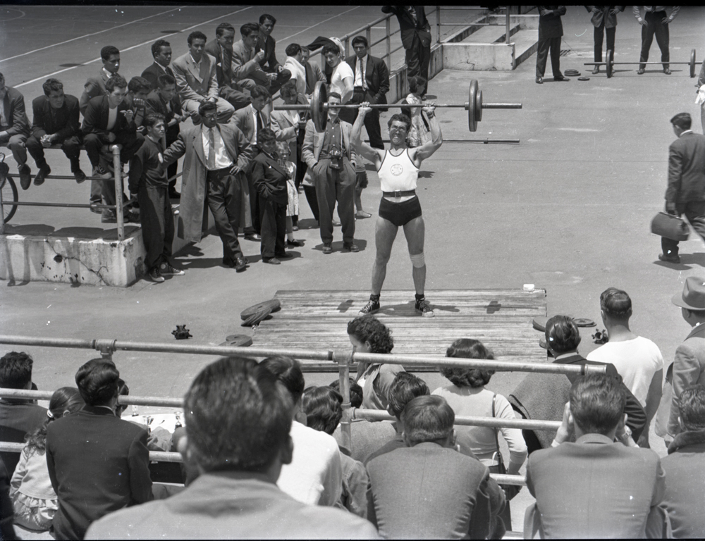 Hombre levantando pesas. La relación entre deportista y público, el contraste marcado por la vestimenta y la separación física de este hombre que enfatiza su carácter peculiar. En Caicedo el deporte también es una excusa para reflexionar sobre diferentes instancias de conformación del espectáculo como marcador de la modernidad.