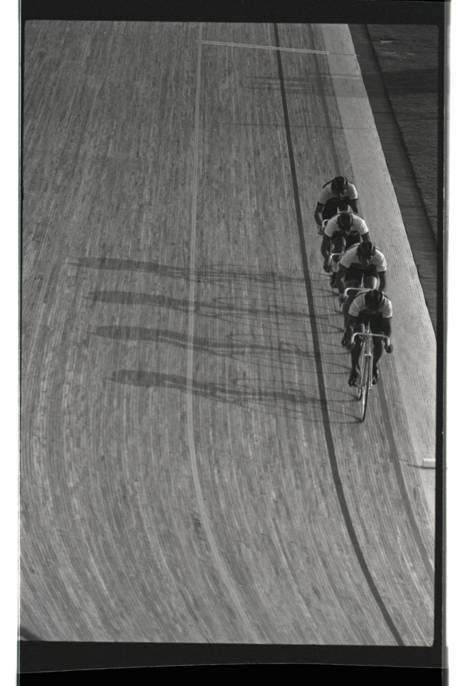 Ciclistas en línea en el velódromo. Esta imagen, sobresaliente en términos composicionales, hace evidente la belleza geométrica que tanto interesó a Caicedo. Los ciclistas en línea en contraste con sus sombras mucho más orgánicas aluden a las demandas de eficiencia que sobre el cuerpo impone el ciclismo de pista y encuentran un correlato en la propia composición de la imagen.