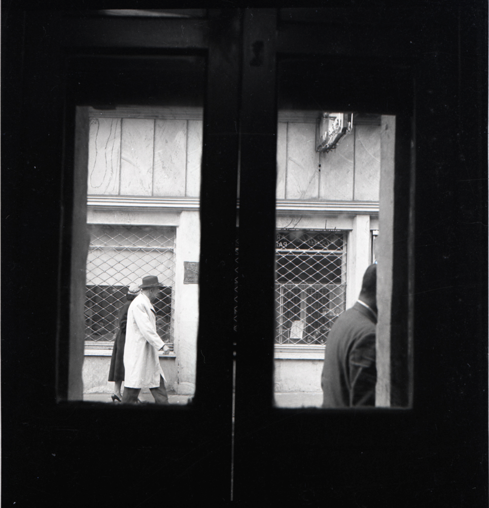 Mirando a través de la ventana, 1956. Una escena urbana enmarcada literalmente por unas puertas de vidrio que separan el mundo público del privado. Esta separación fascinó a Caicedo durante su labor fotográfica y los marcos de ventanas, puertas, pasadizos, fueron empleados repetidamente para resaltarla y problematizarla.