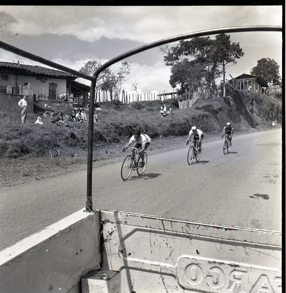 Ciclismo, Vuelta a Colombia, 1969. Negativo de 6x6 cm. Los marcos como herramientas de composición en la fotografía fueron empleados ampliamente por Caicedo. En esta imagen sirven como principio composicional que captura una escena particular de una de sus grandes pasiones fotográficas, el ciclismo, particularmente la Vuelta a Colombia.